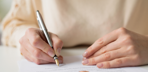 Close-up of a woman signing a legal document with wedding rings placed on the paper.