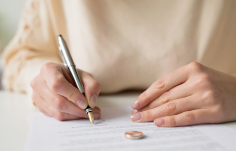 Close-up of a woman signing a legal document with wedding rings placed on the paper.
