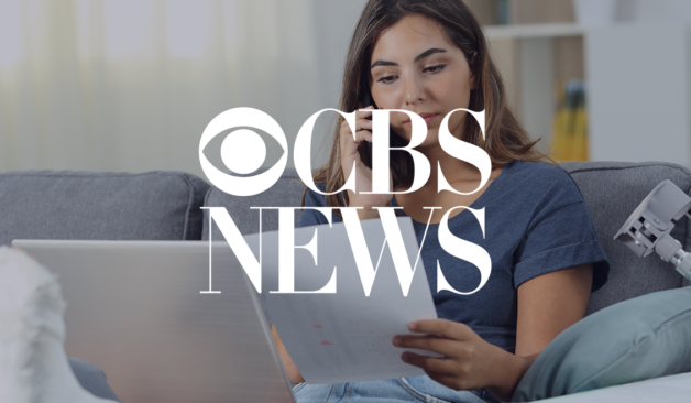 Young woman sitting on a couch looking at paperwork and speaking on the phone, with CBS News logo overlaid.