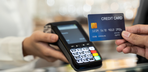 Person holding a credit card near a payment terminal for contactless transaction.