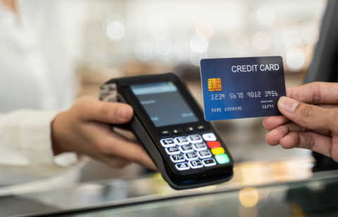 Person holding a credit card near a payment terminal for contactless transaction.