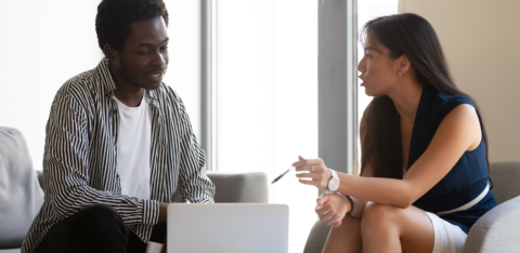 Man and woman sitting on couches having a focused conversation with a laptop open between them