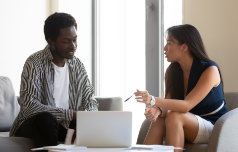 Man and woman sitting on couches having a focused conversation with a laptop open between them