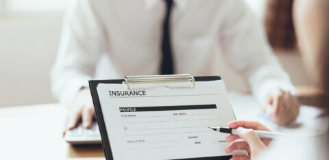 Close-up of a person filling out a health insurance form on a clipboard during a meeting.