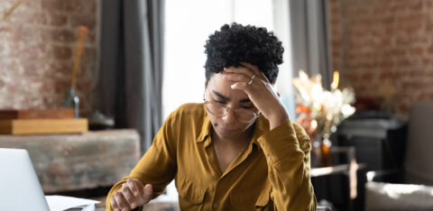 Person sitting at a desk looking stressed while reviewing documents with a laptop and calculator nearby