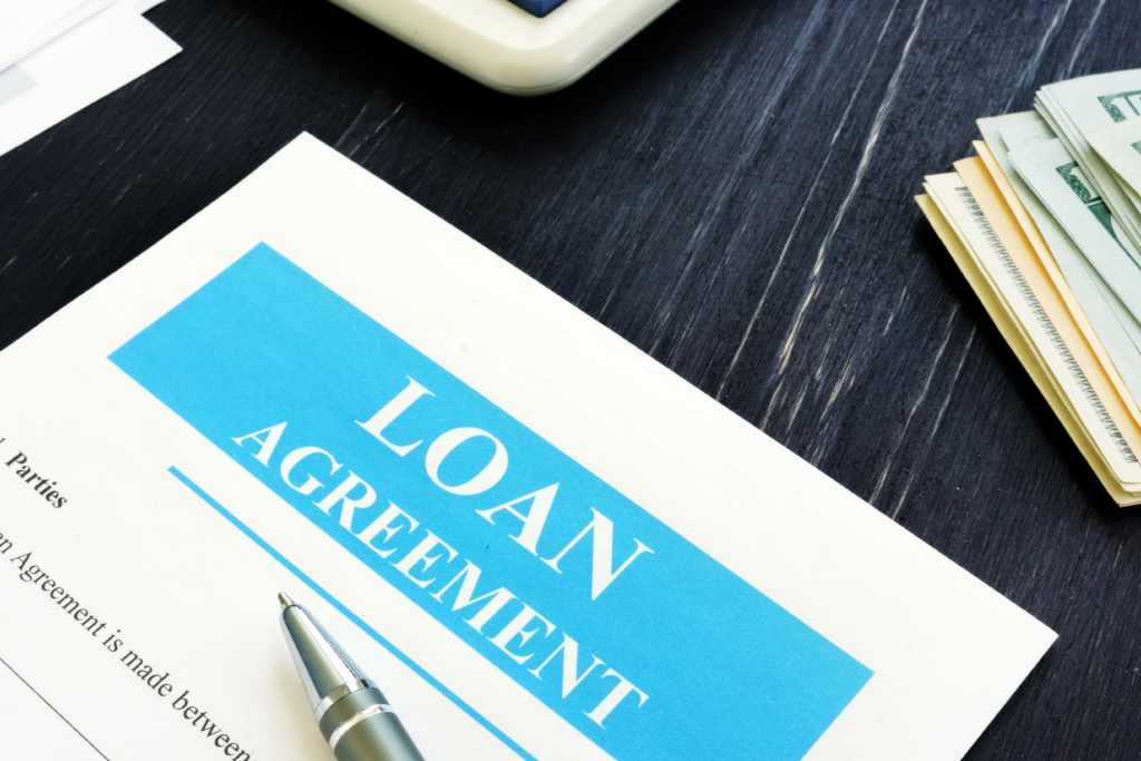 Close-up of a loan agreement document on a desk with a pen, cash, and calculator nearby.