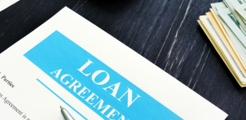 Close-up of a loan agreement document on a desk with a pen, cash, and calculator nearby.