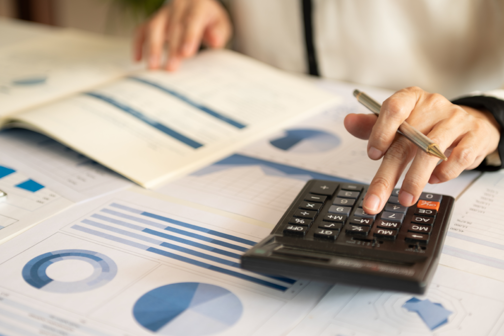 Person using a calculator and reviewing financial charts and graphs on printed documents.