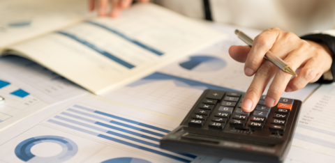 Person using a calculator and reviewing financial charts and graphs on printed documents.