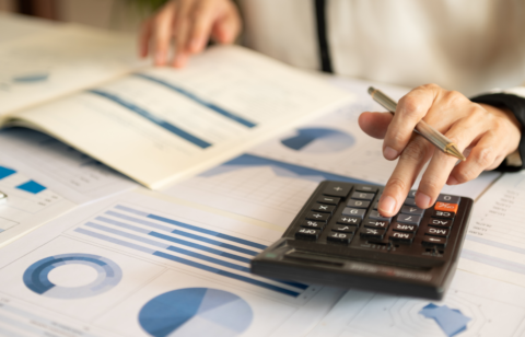 Person using a calculator and reviewing financial charts and graphs on printed documents.