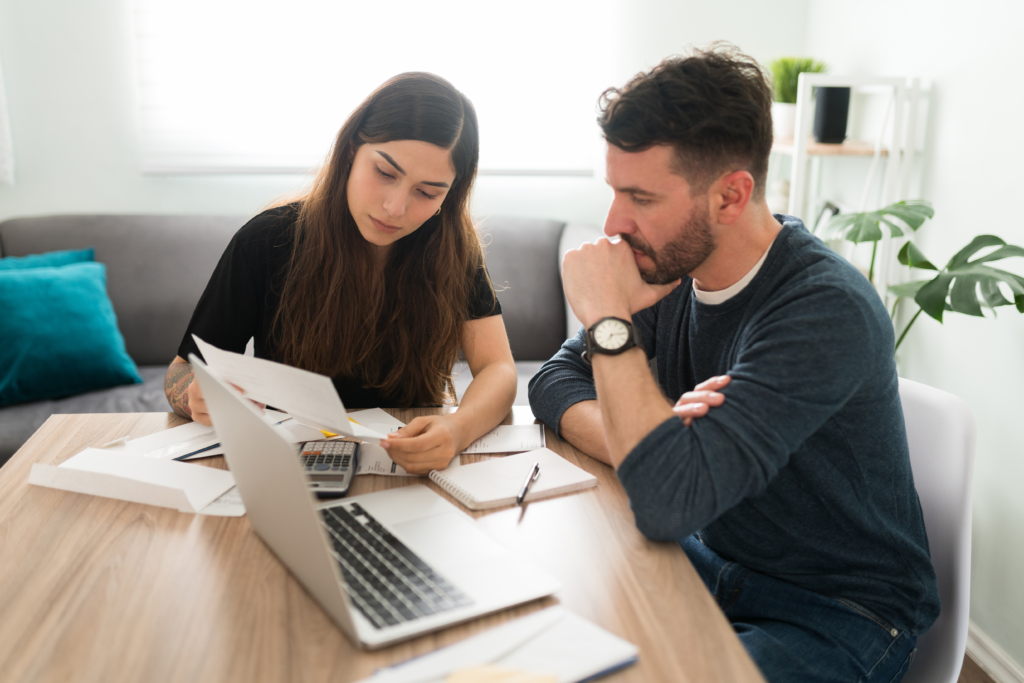 Couple sitting at a table reviewing financial documents with a laptop and calculator.