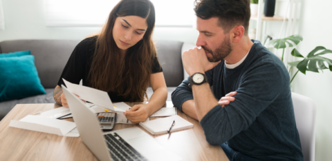 Couple sitting at a table reviewing financial documents with a laptop and calculator.