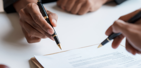 Two people holding pens while reviewing and signing a document on a clipboard.
