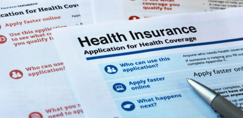 Close-up of health insurance application forms with a pen resting on one of the pages.