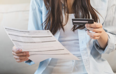 Woman reviewing a bill or financial statement while holding a credit card, seated indoors.