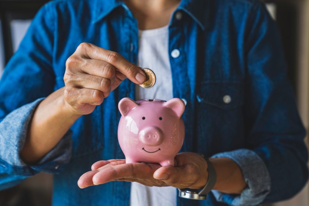 Person placing a coin into a pink piggy bank while holding it in their hand.