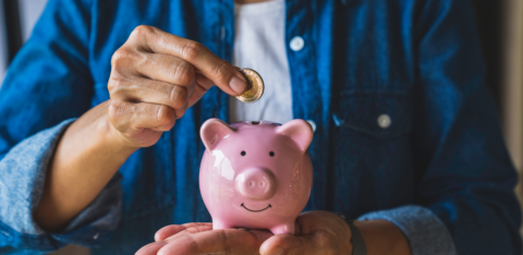 Person placing a coin into a pink piggy bank while holding it in their hand.