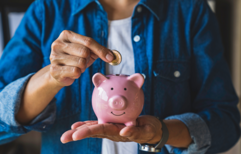 Person placing a coin into a pink piggy bank while holding it in their hand.