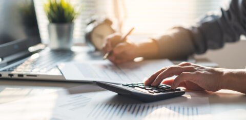 Person using a calculator and reviewing financial documents at a desk with a laptop.