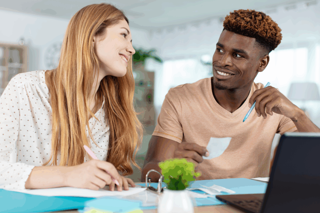 Smiling couple working together at a table with papers, receipts, and a laptop, possibly budgeting or reviewing finances.