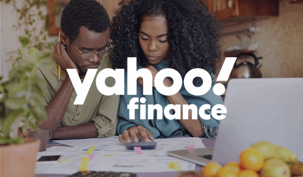 A couple reviews financial documents together at a kitchen table, using a calculator and laptop, with “Yahoo Finance” logo overlay.