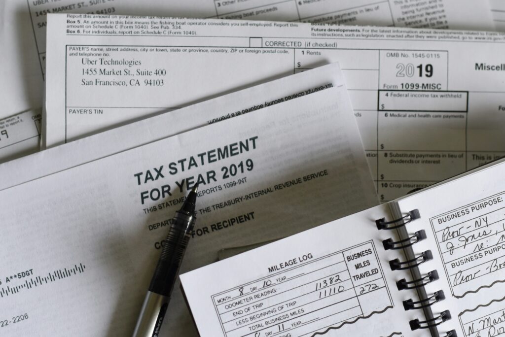A collection of 2019 tax documents, including a 1099-MISC form from Uber Technologies, a tax statement envelope, a pen, and a mileage log notebook showing business miles traveled.