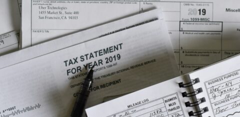 A collection of 2019 tax documents, including a 1099-MISC form from Uber Technologies, a tax statement envelope, a pen, and a mileage log notebook showing business miles traveled.