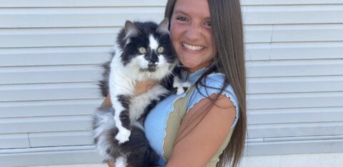 Young woman outdoors holding a fluffy cat, both looking at the camera