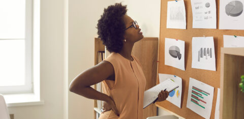 A woman holding a notebook studies charts and graphs pinned to a corkboard in an office.