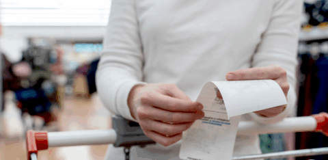 Person reviewing a shopping receipt while standing behind a cart in a store.