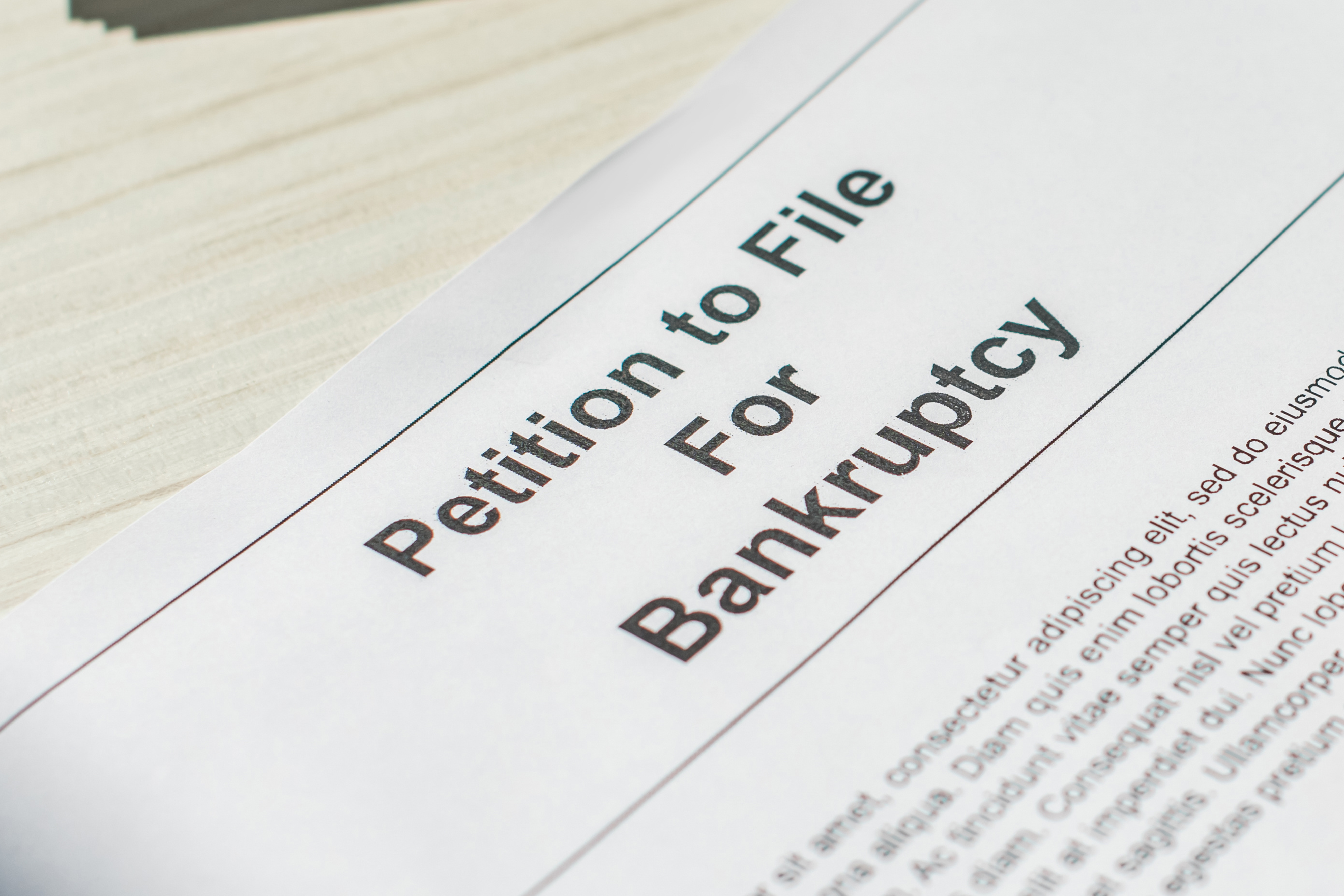 Close-up of a legal document titled “Petition to File for Bankruptcy” on a wooden desk.