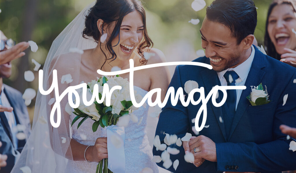 A bride and groom smiling as they walk down the aisle together, surrounded by guests throwing white flower petals. YourTango logo overlayed.