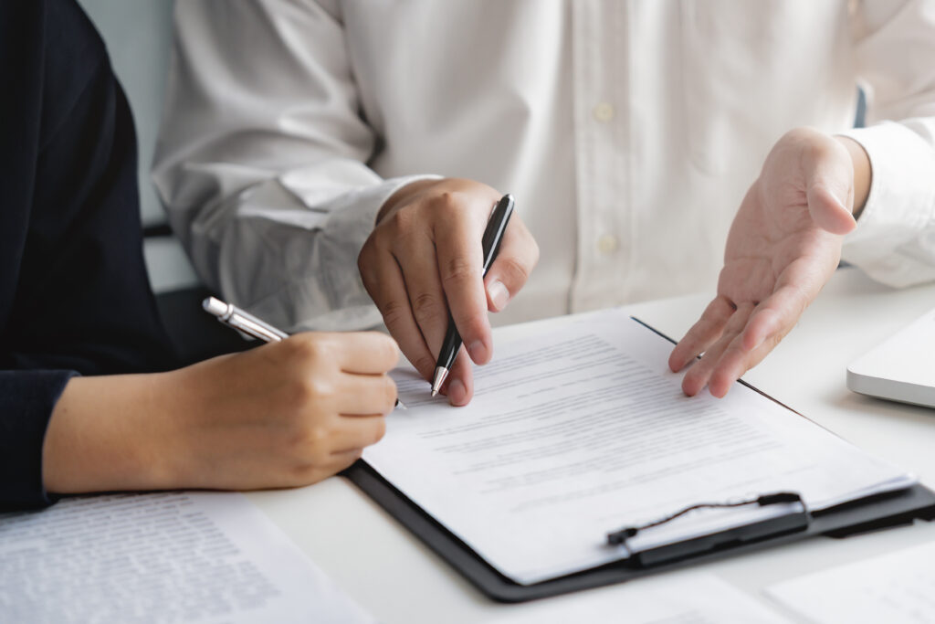 lose-up of two people reviewing and signing a contract on a clipboard at a desk.