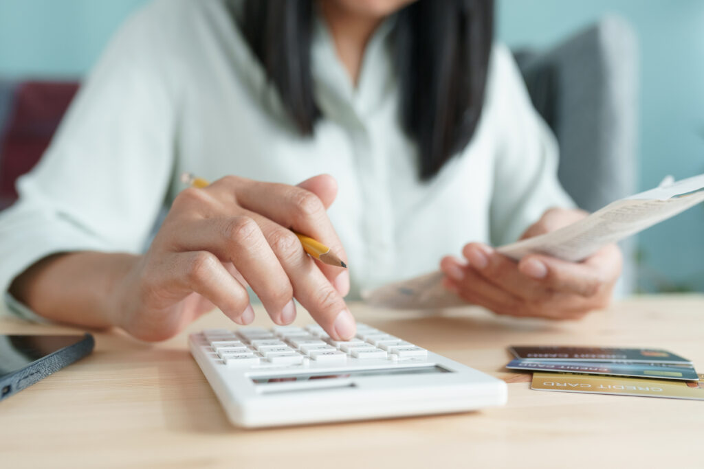 Person using a calculator while holding a receipt, with credit cards and a smartphone nearby.