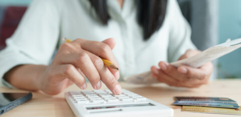 Person using a calculator while holding a receipt, with credit cards and a smartphone nearby.