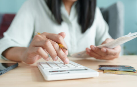 Person using a calculator while holding a receipt, with credit cards and a smartphone nearby.