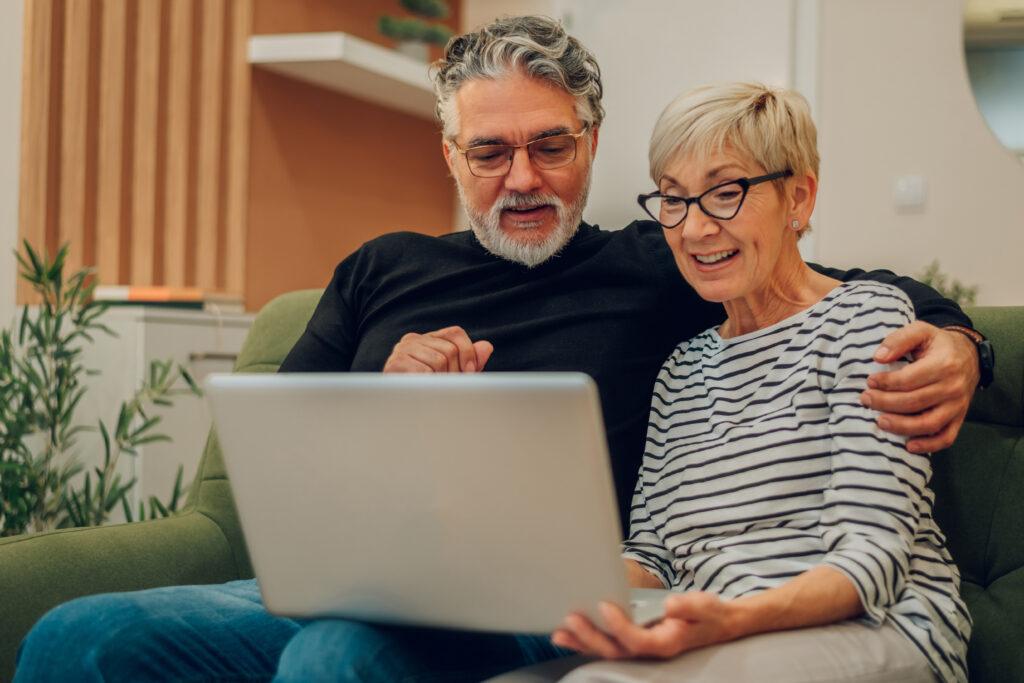 Smiling older couple sitting on a couch, looking at a laptop together.