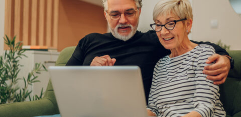 Smiling older couple sitting on a couch, looking at a laptop together.