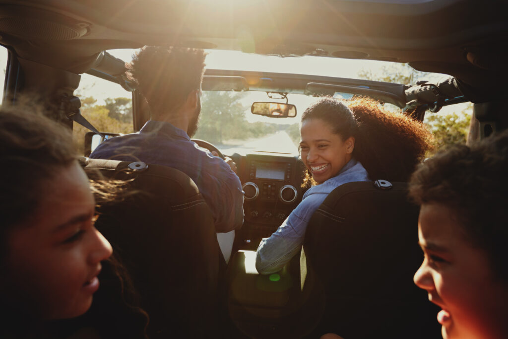 Family enjoying a road trip in a car with the mother smiling back at her children.