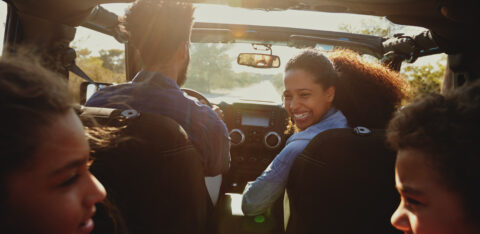 Family enjoying a road trip in a car with the mother smiling back at her children.