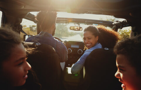 Family enjoying a road trip in a car with the mother smiling back at her children.