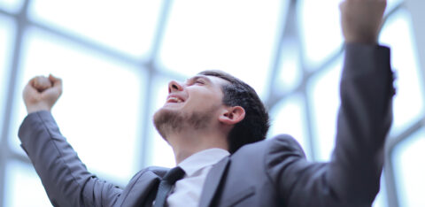 Young man in a suit cheering with arms lifted, expressing joy and success.