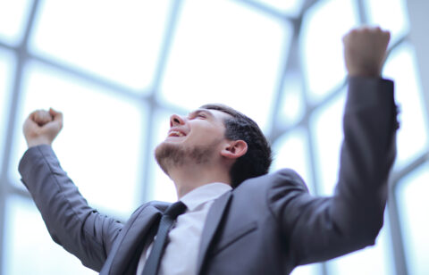 Young man in a suit cheering with arms lifted, expressing joy and success.