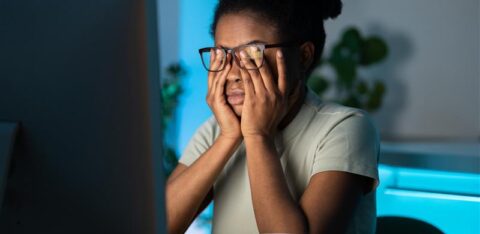 Woman sitting at a desk holding her face in frustration while looking at a computer screen.