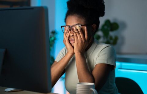 Woman sitting at a desk holding her face in frustration while looking at a computer screen.