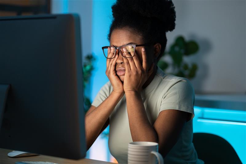 Woman sitting at a desk holding her face in frustration while looking at a computer screen.