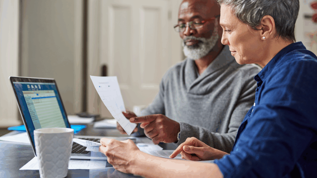 Older couple reviewing financial documents together at a table with a laptop.