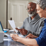 Older couple reviewing financial documents together at a table with a laptop.