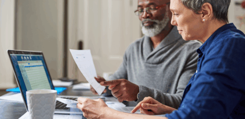 Older couple reviewing financial documents together at a table with a laptop.