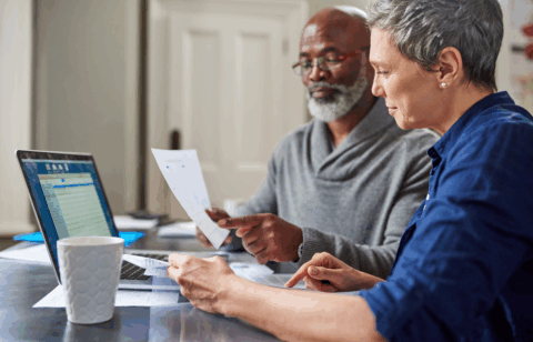 Older couple reviewing financial documents together at a table with a laptop.